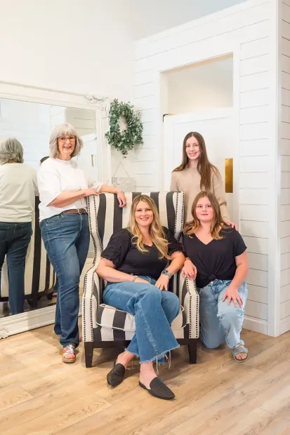 Four women posing in a bright white retail showroom with mirrors and a potted plant