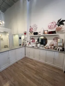 Elegant vanity room with white cabinets, round mirror, pink floral decor, and wood flooring