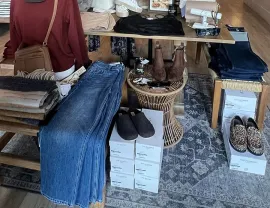 Clothing and accessories display on rugs: jeans, boots, shoes, and folded garments on wooden tables