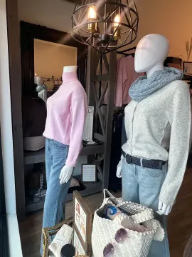Two mannequins in a boutique window display, one in pink sweater and jeans, one in gray sweater and scarf.