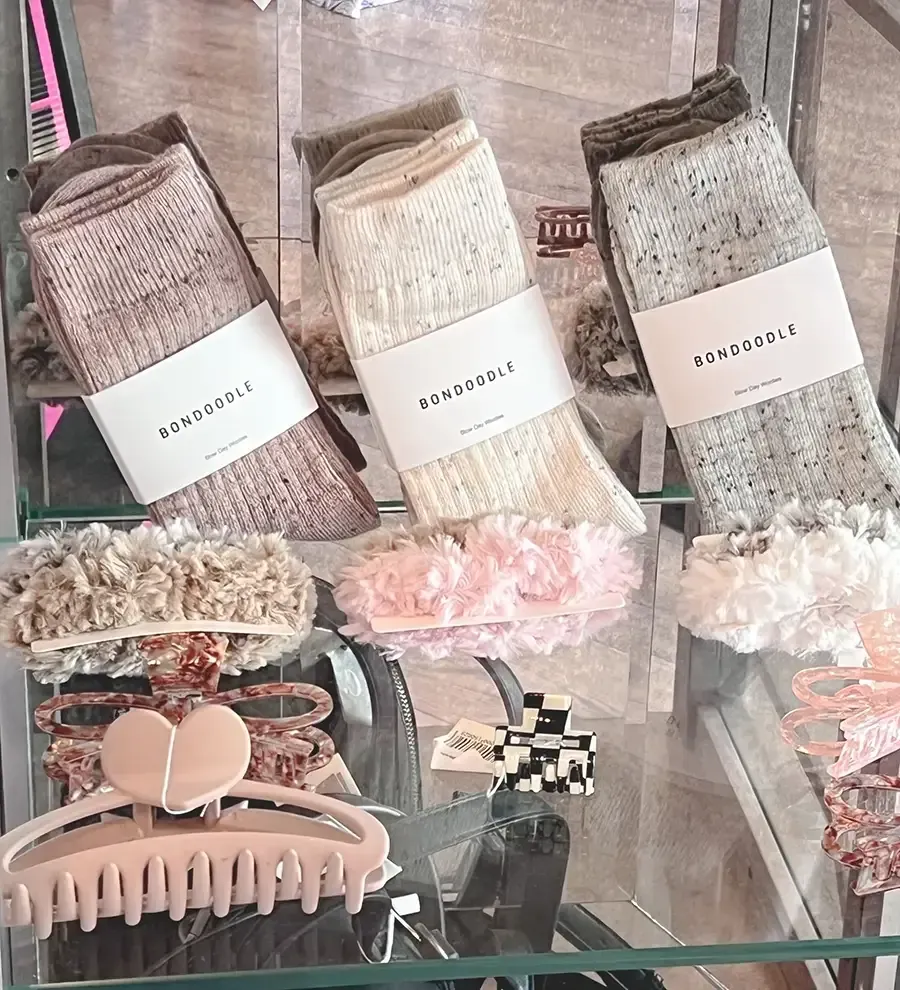 Three patterned socks on a glass shelf, with hair clips and pastel accessories below