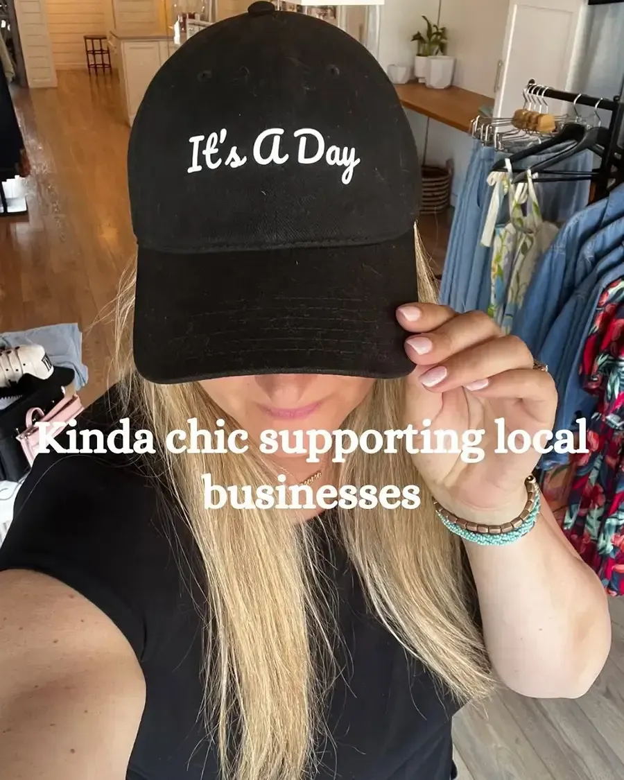 Woman in black cap and top taking a selfie in a clothing shop, with text overlay about supporting local businesses