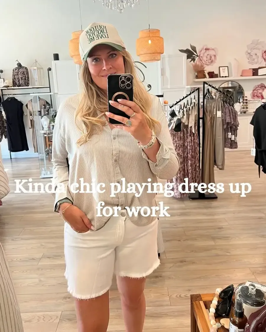 Woman taking a mirror selfie in a clothing boutique, wearing a white outfit and cap.