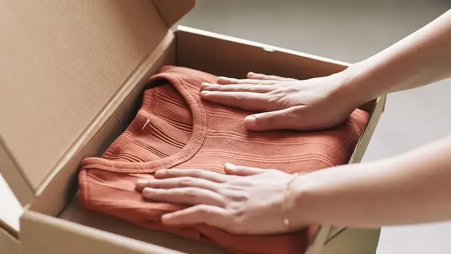 Hands folding a coral sweater in a cardboard box