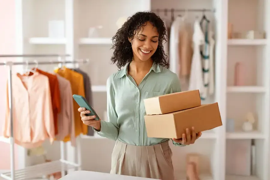 Woman packing boxes while holding a phone in a clothing boutique
