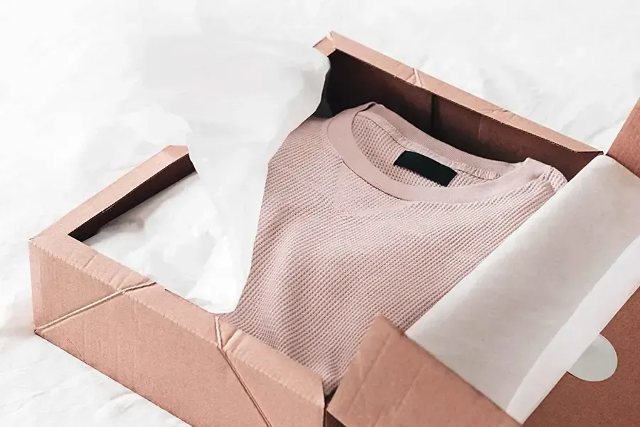 Folded pink sweater in an open cardboard box with white tissue paper