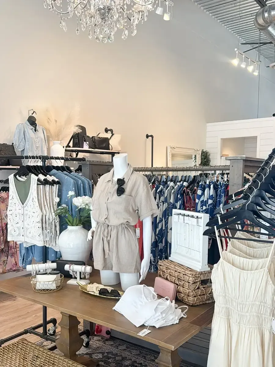 Boutique clothing display with white dresses, racks of apparel, and a wooden table in a bright showroom