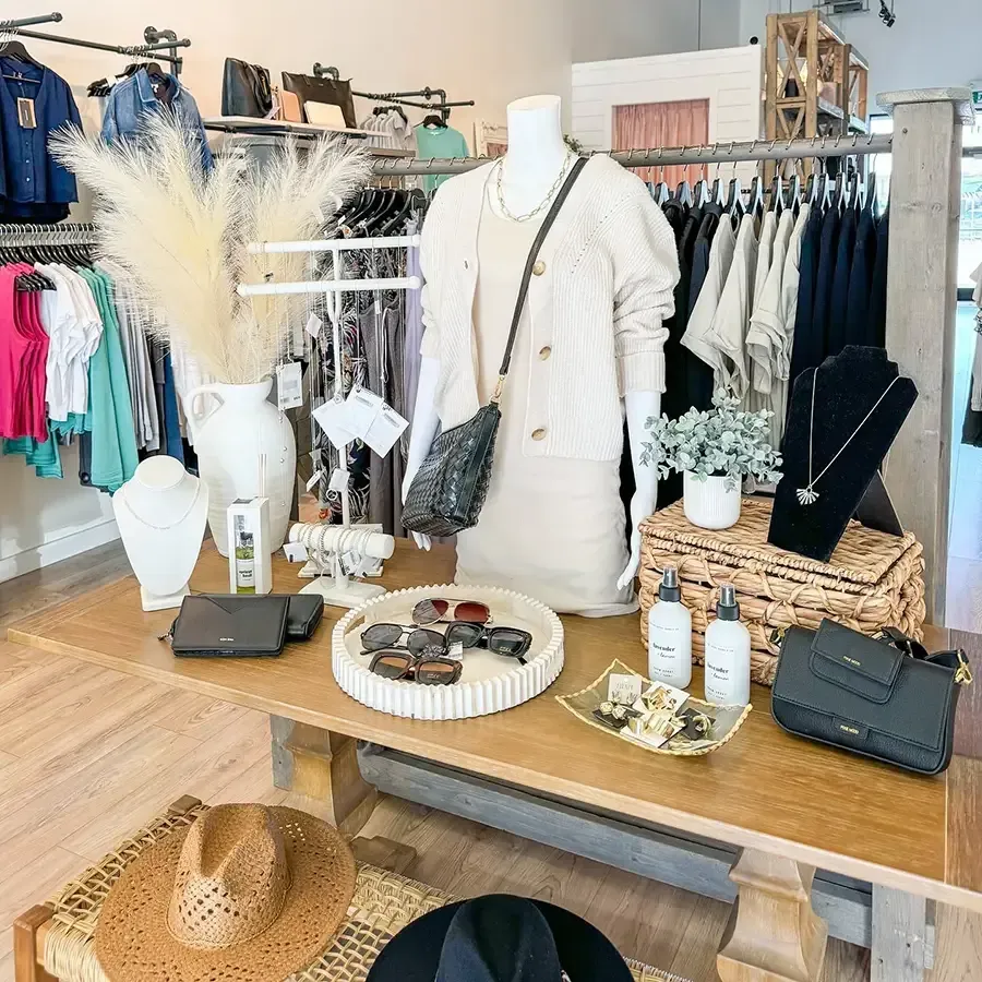 Boutique display table with white clothing, accessories, hats, and small decor items in a bright shop
