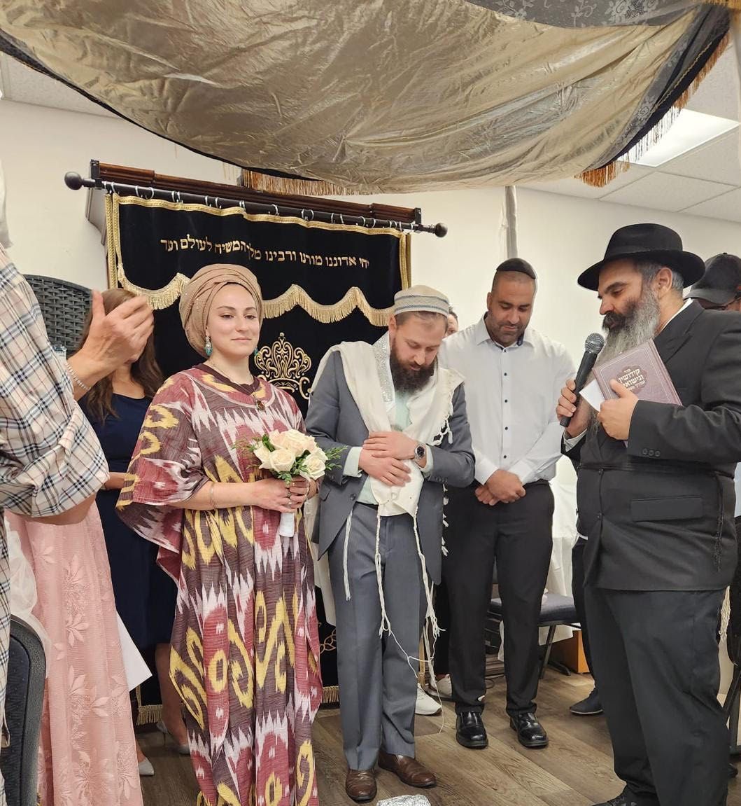 Jewish wedding ceremony with couple under a chuppah. A Rabbi with a book leads ceremony.