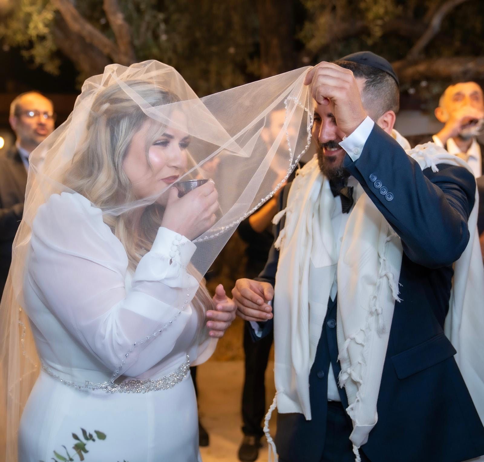 Jewish wedding: Bride drinking wine under veil as groom lifts it.