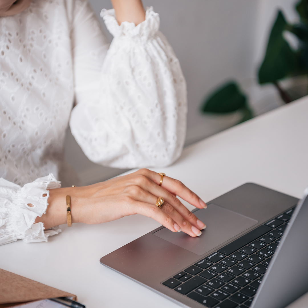Woman in white blouse using a laptop, resting hand on touchpad.