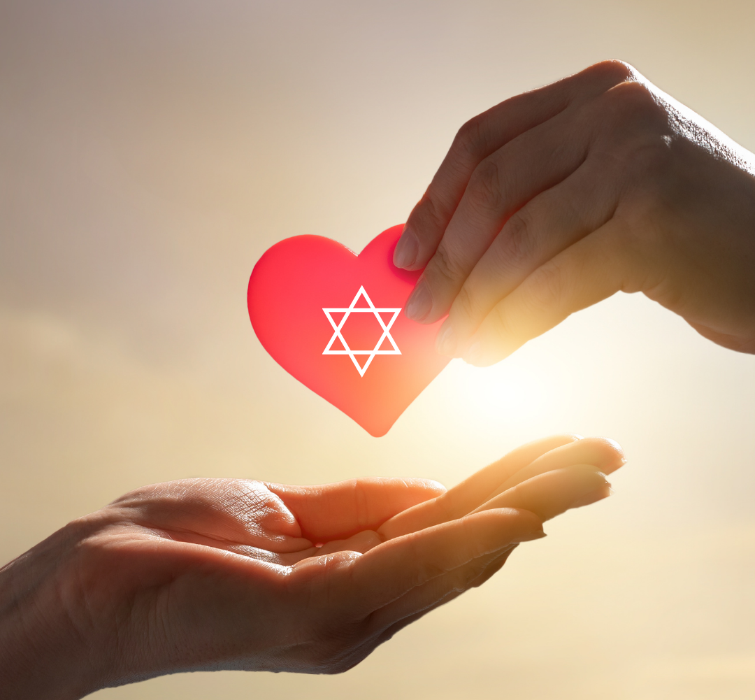 Hands passing a red heart with a Star of David, backlit by sunlight.