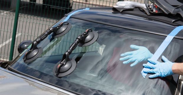 Hands in blue gloves clean the windshield of a black car with suction cups attached.