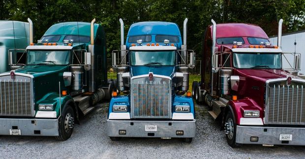 Three colorful semi trucks parked side by side on a gravel lot