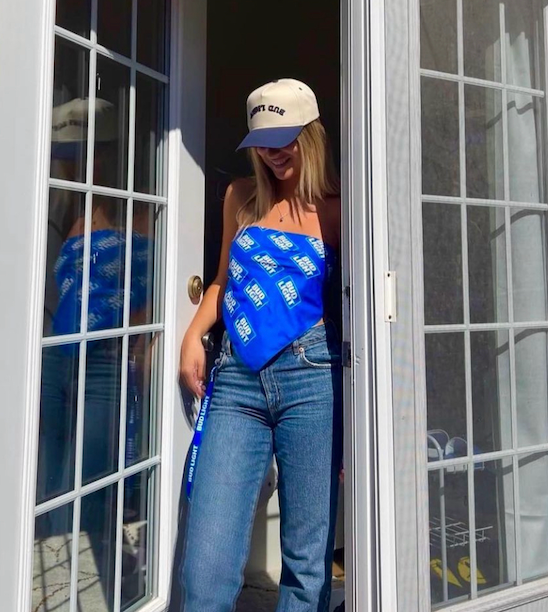 A woman wearing a hat and a blue scarf is standing in a doorway.