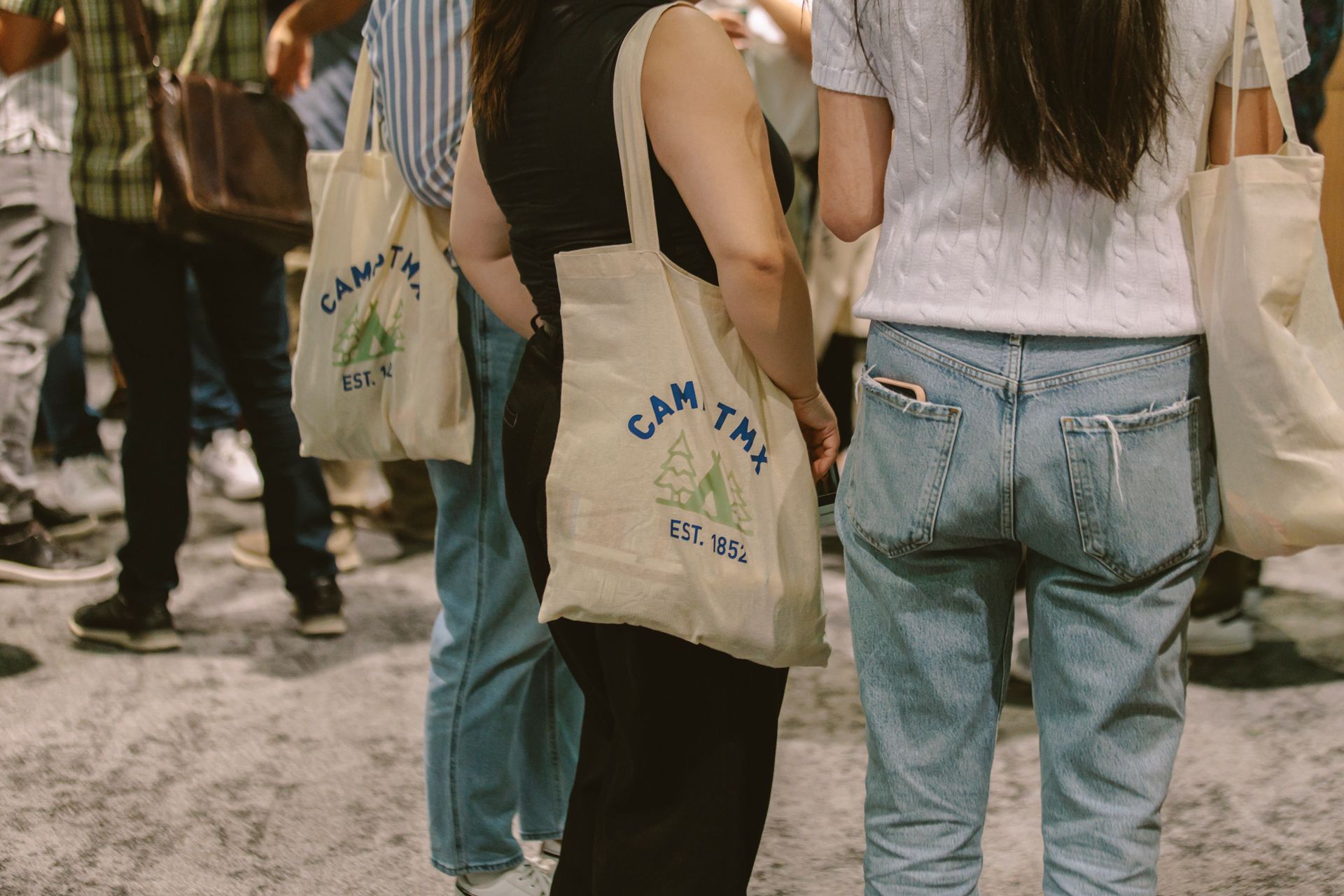A group of people are standing in a line holding tote bags.