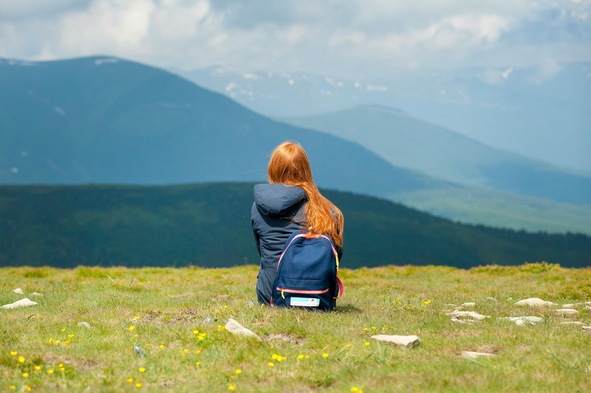 A woman with a backpack is sitting on top of a grassy hill.