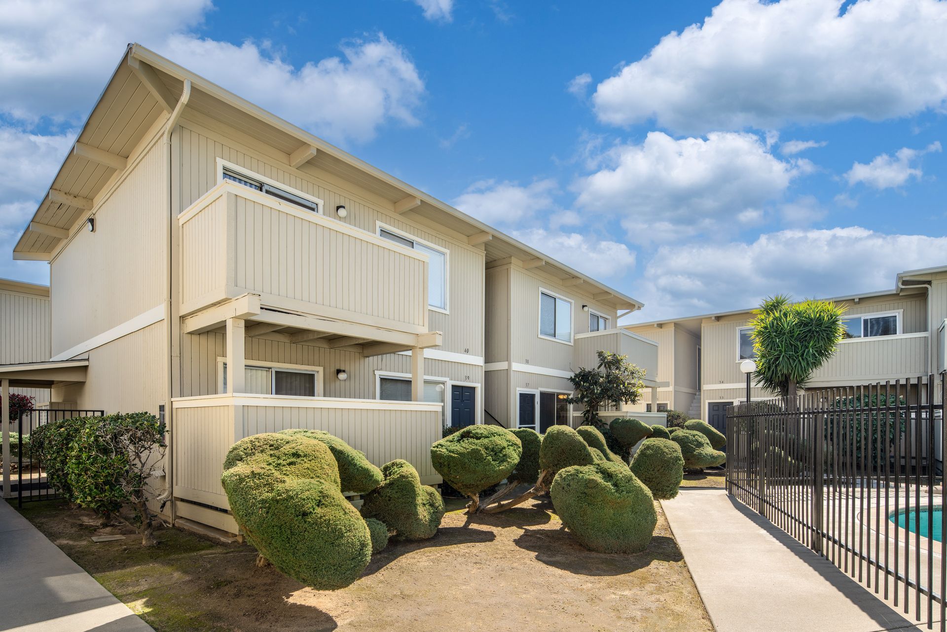 Apartment building with tan siding and balconies, under a blue sky with puffy clouds.