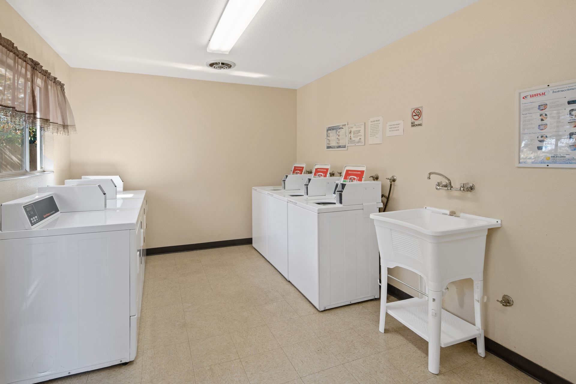 Laundry room with white machines, beige walls, and a utility sink.