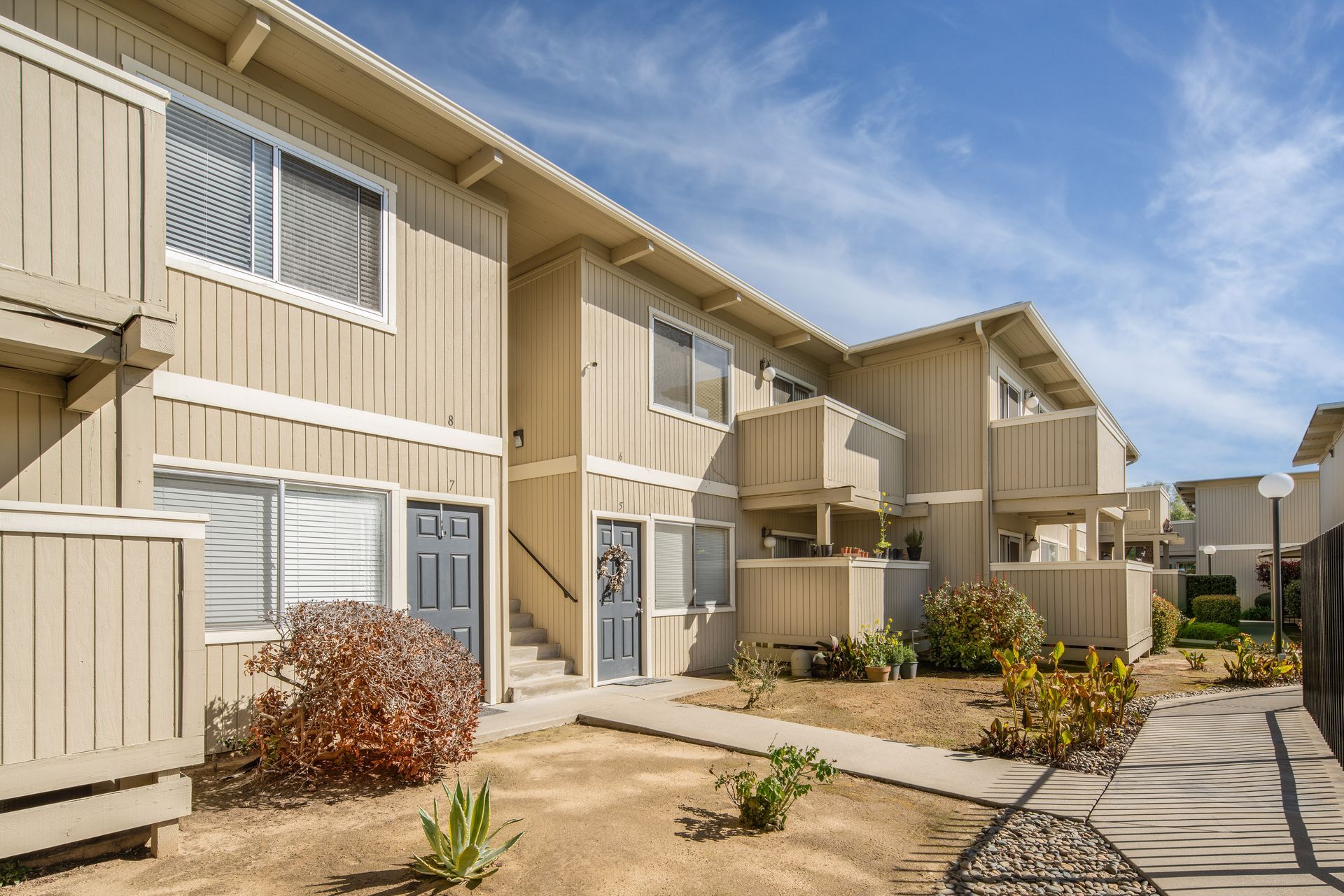 Beige apartment complex exterior with balconies, blue doors, and a sunny sky.