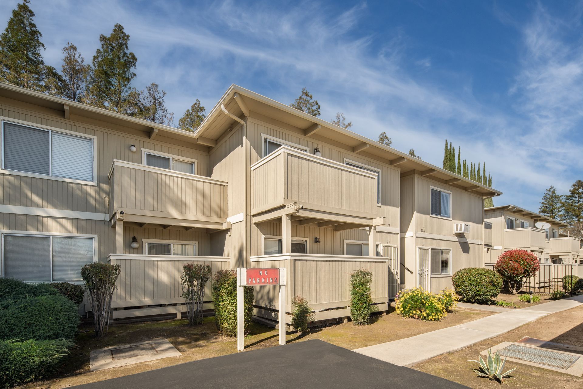Apartment complex exterior with balconies, tan siding, and landscaping under a blue sky.