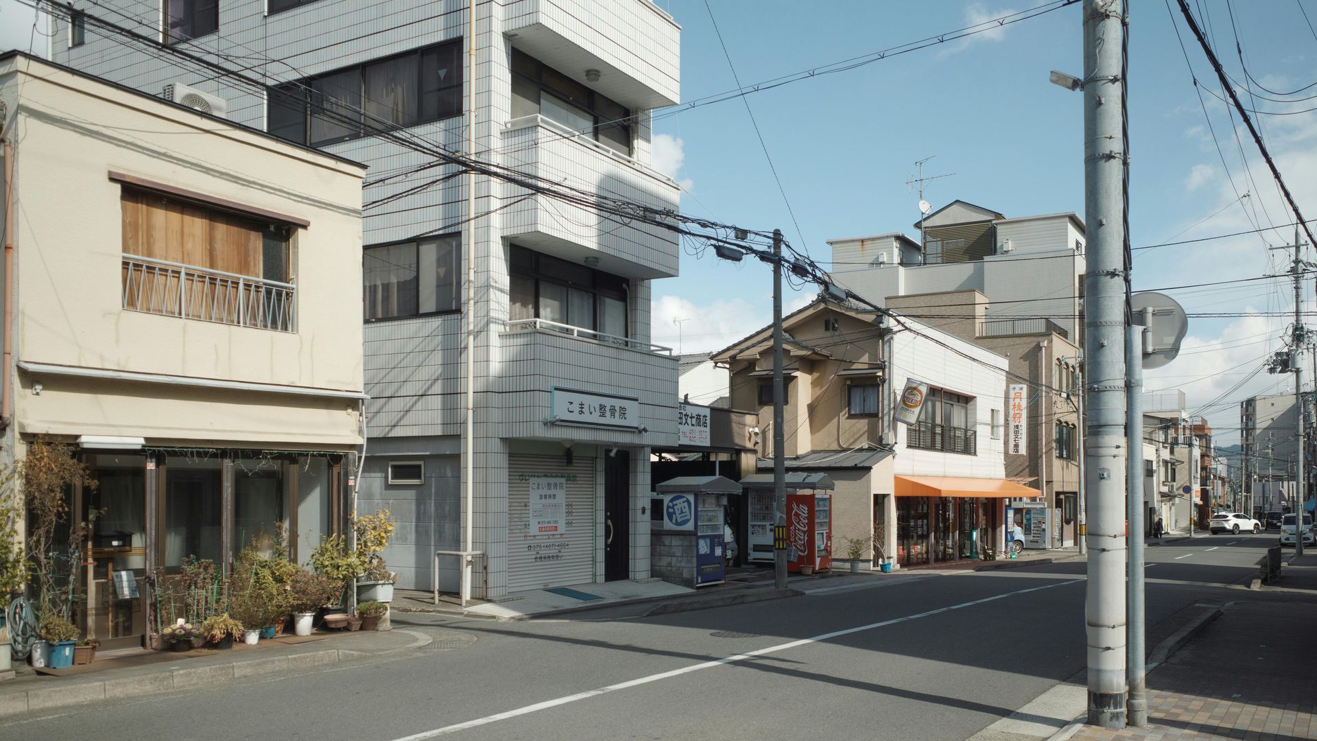 Street scene in Japan with buildings, power lines, and a clear sky.