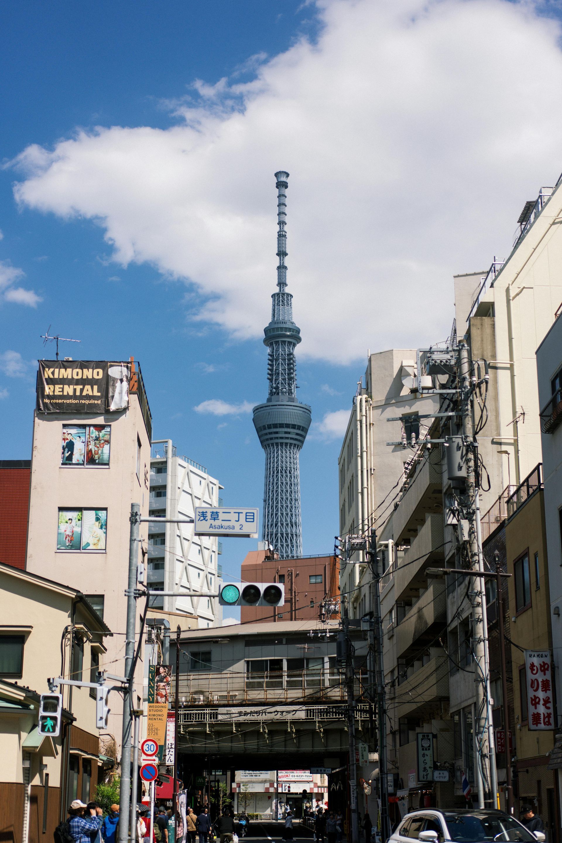 Tokyo Skytree towering over a street lined with buildings and overhead power lines under a blue sky.