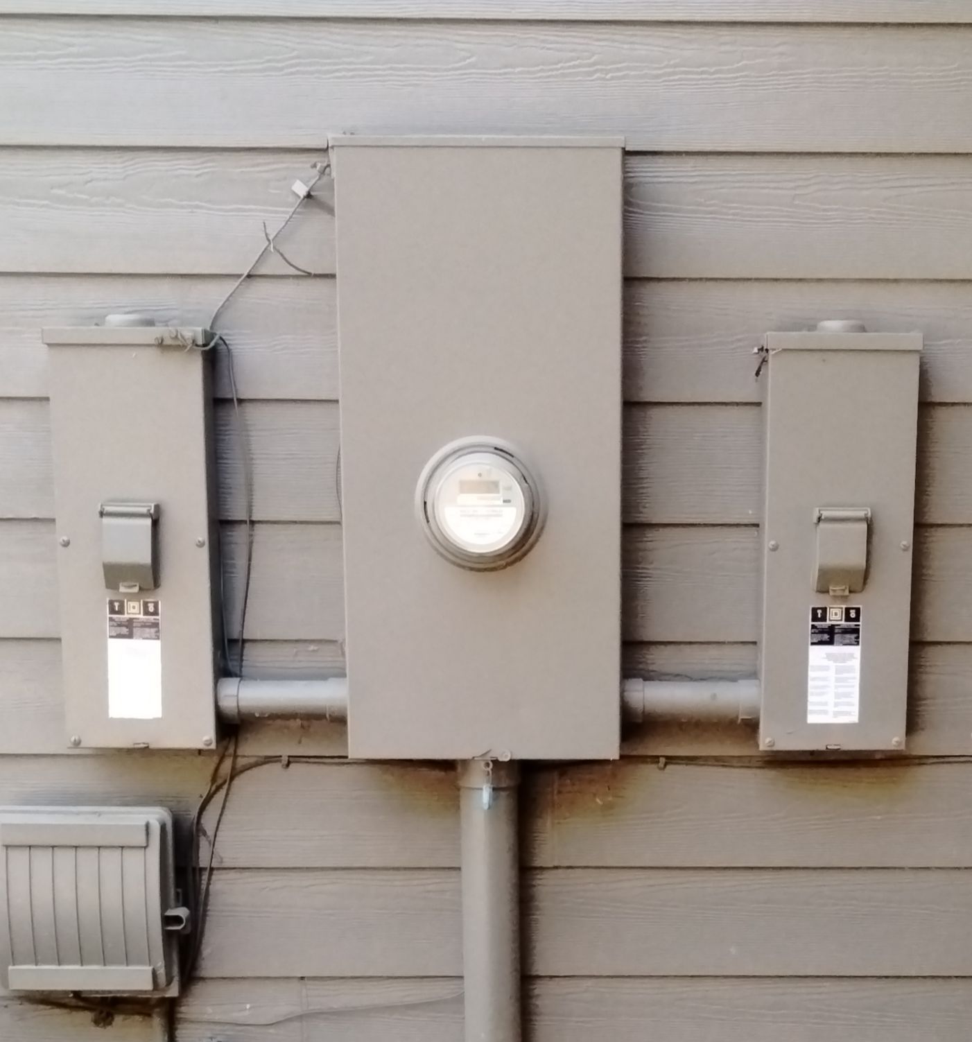 Three gray utility meters mounted on an exterior house wall, with a round meter in the center.