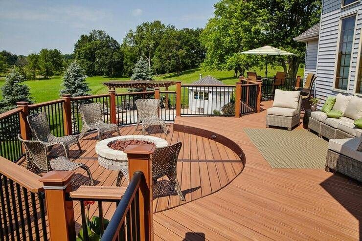 Spacious wooden deck with fire pit, seating areas, and a view of green fields under a sunny sky. Spacious wooden deck with fire pit, seating areas, and a view of green fields under a sunny sky.