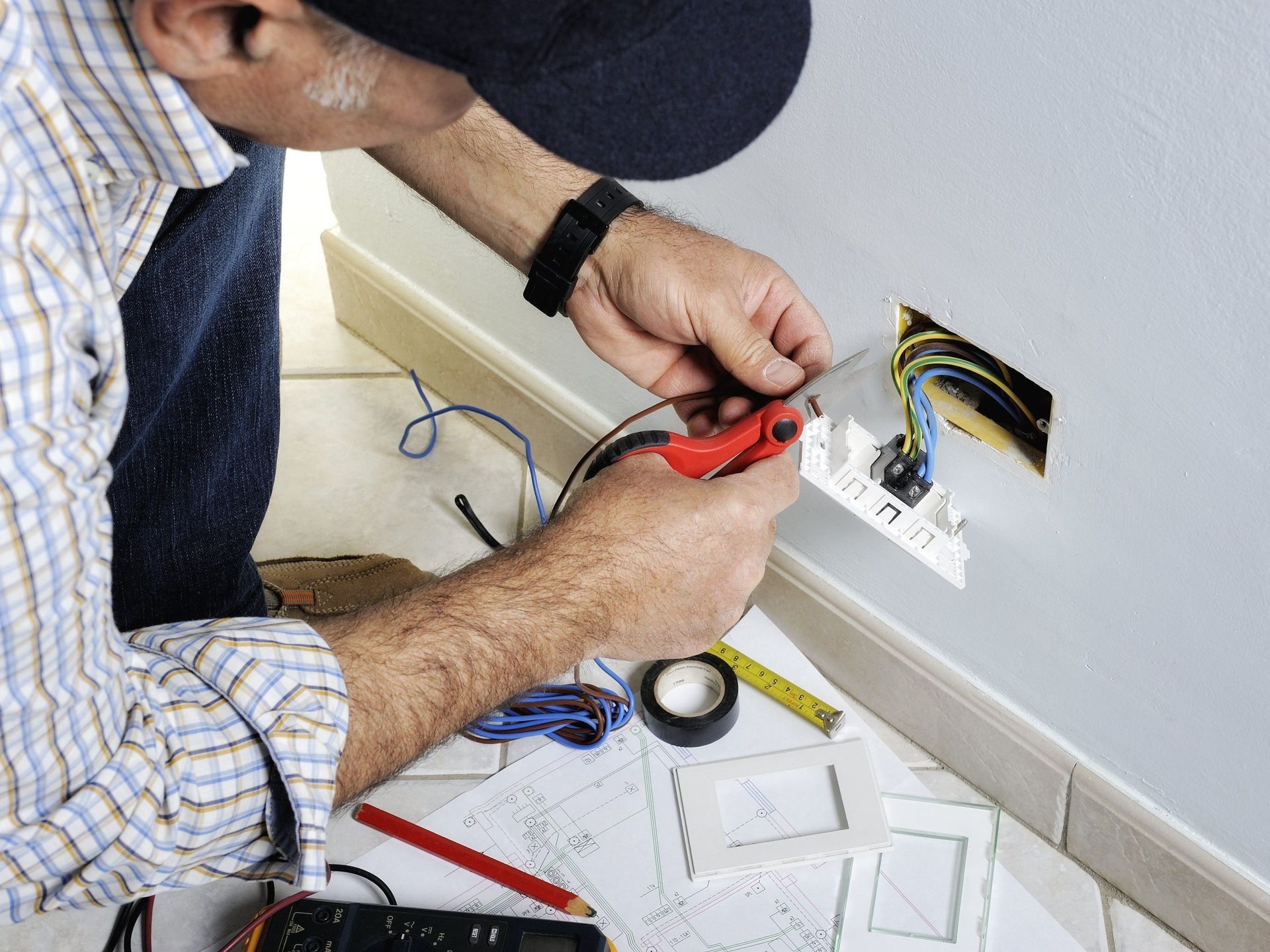 Electrician connecting wires in a wall outlet box with a red-handled tool. Electrician connecting wires in a wall outlet box with a red-handled tool.