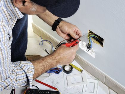 Electrician connecting wires in a wall outlet box with a red-handled tool. Electrician connecting wires in a wall outlet box with a red-handled tool.