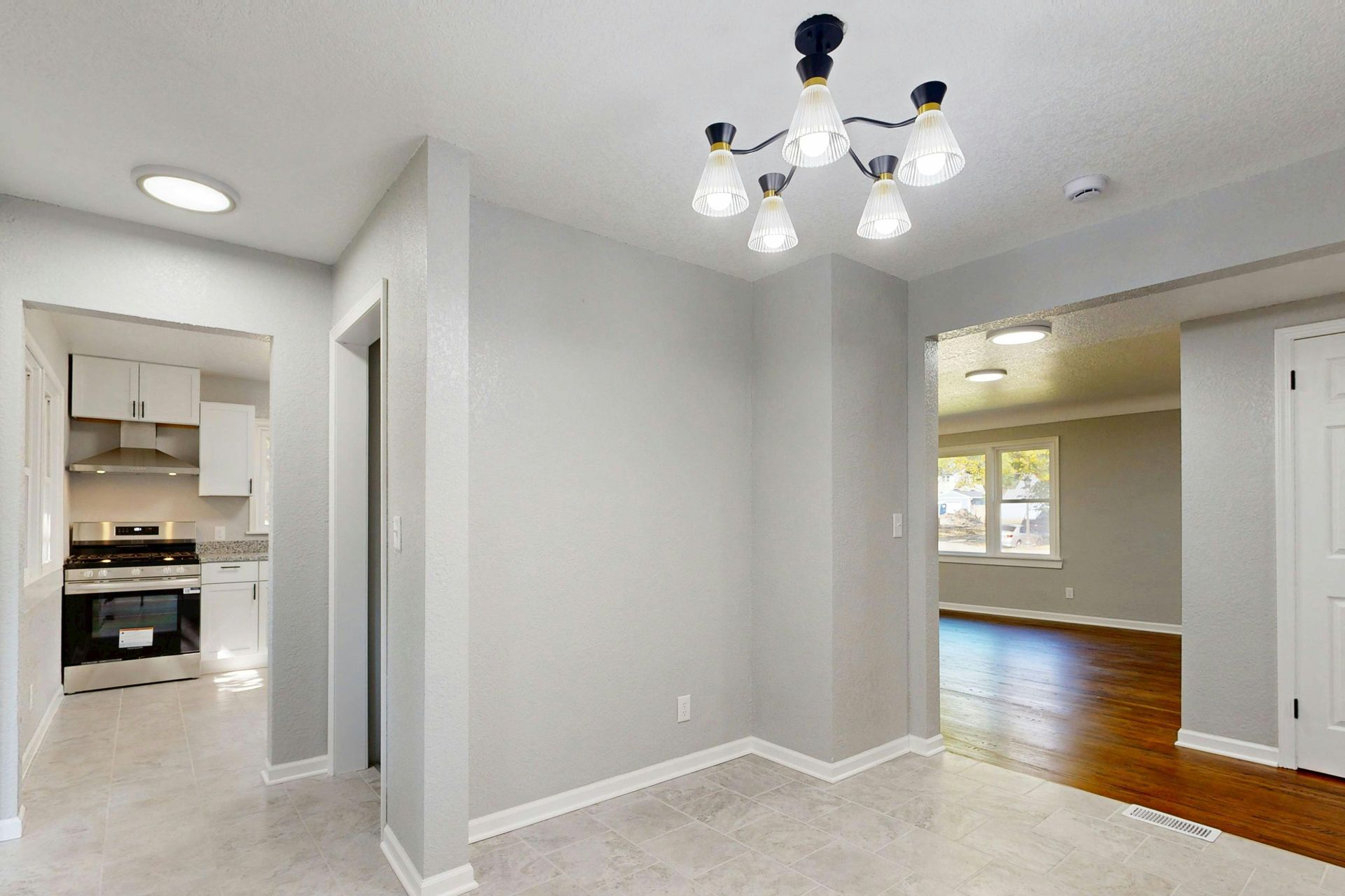 Empty white dining area with carpet, chandelier, and view into a kitchen and hardwood-floored room Empty white dining area with carpet, chandelier, and view into a kitchen and hardwood-floored room