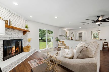 Bright open living room with a white fireplace, beige sofa, and view into a kitchen and dining area Bright open living room with a white fireplace, beige sofa, and view into a kitchen and dining area