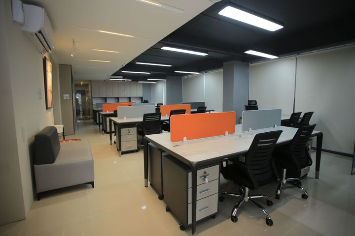Modern open office with desks, black chairs, orange privacy panels, and overhead lighting