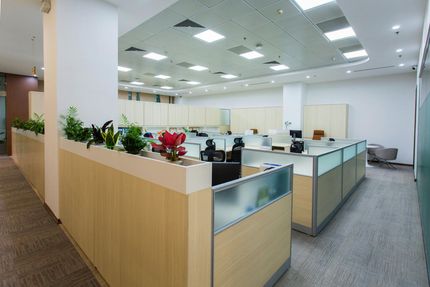 Open-plan office with cubicles, desks, and potted plants under bright ceiling lights. Open-plan office with cubicles, desks, and potted plants under bright ceiling lights.