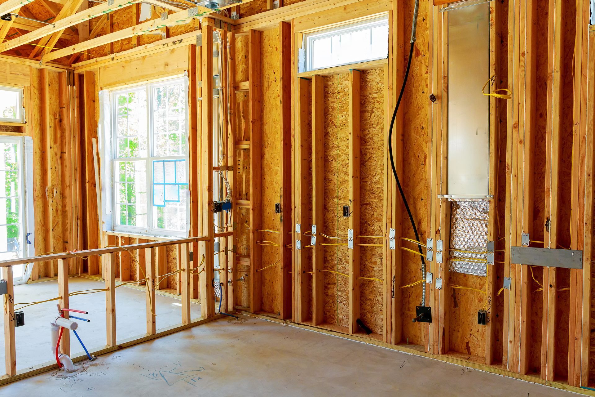 Unfinished room with exposed wooden framing, insulation, windows, and a concrete floor under construction. Unfinished room with exposed wooden framing, insulation, windows, and a concrete floor under construction.