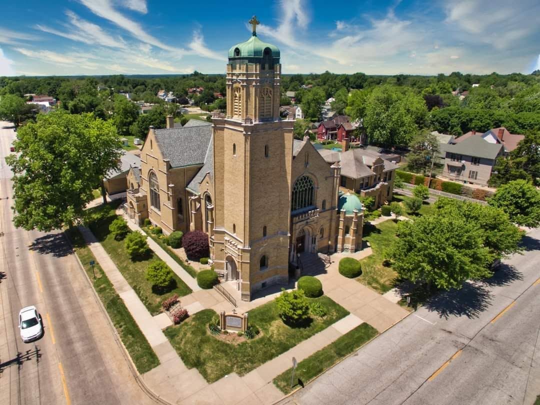 Aerial view of a stone church with a green dome, surrounded by trees and neighborhood streets.