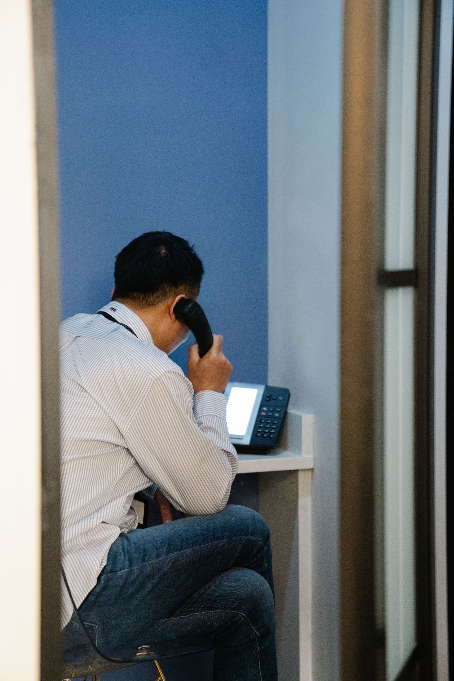 Person seated at a desk, speaking on a phone in a small office cubicle.