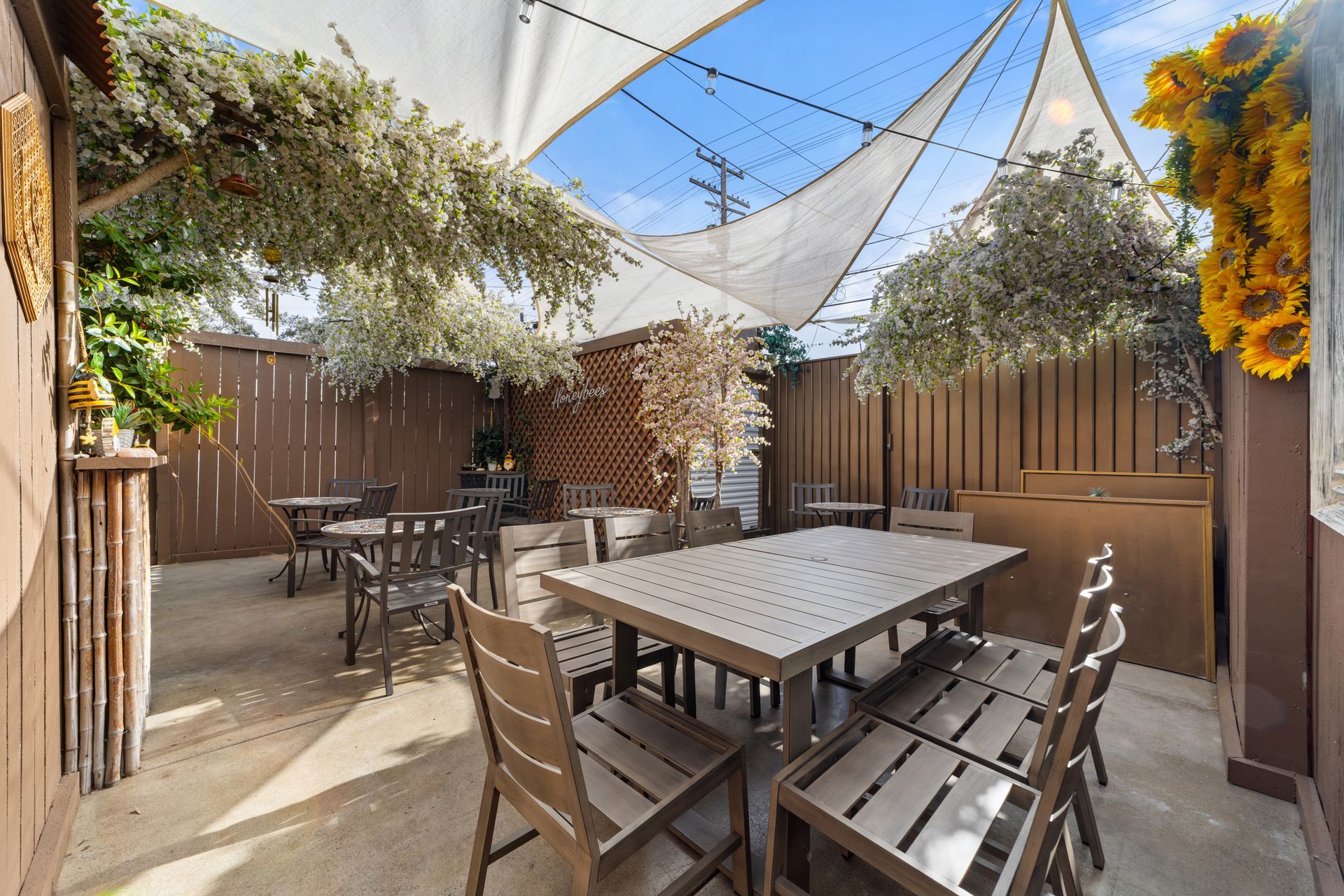 Outdoor patio with shaded seating, decorated with flowers and a wood fence.