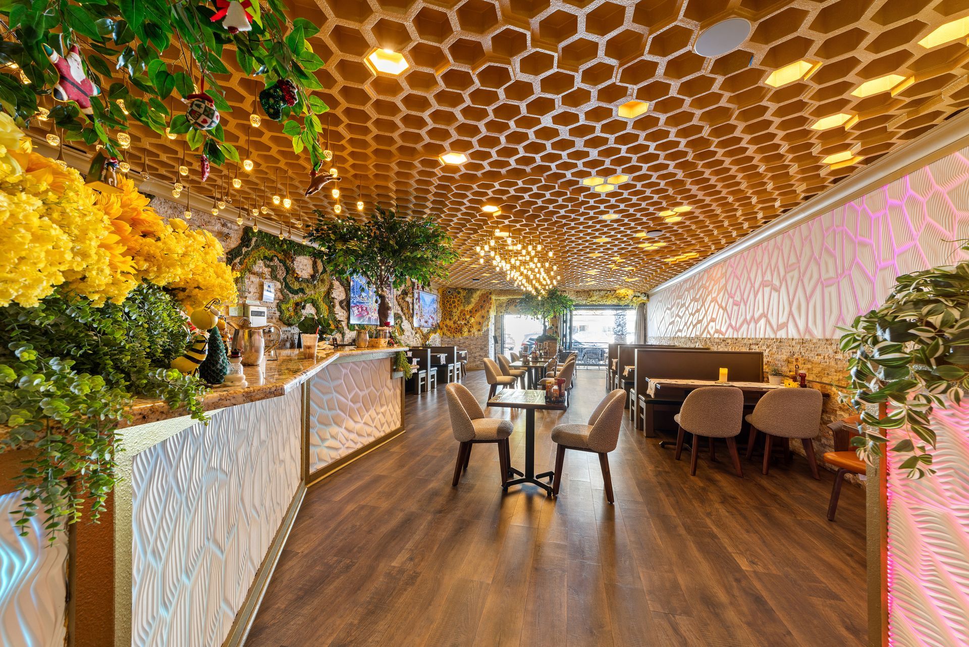 Restaurant interior with honeycomb ceiling, floral decorations, and seating. Wooden floors and textured walls are visible.