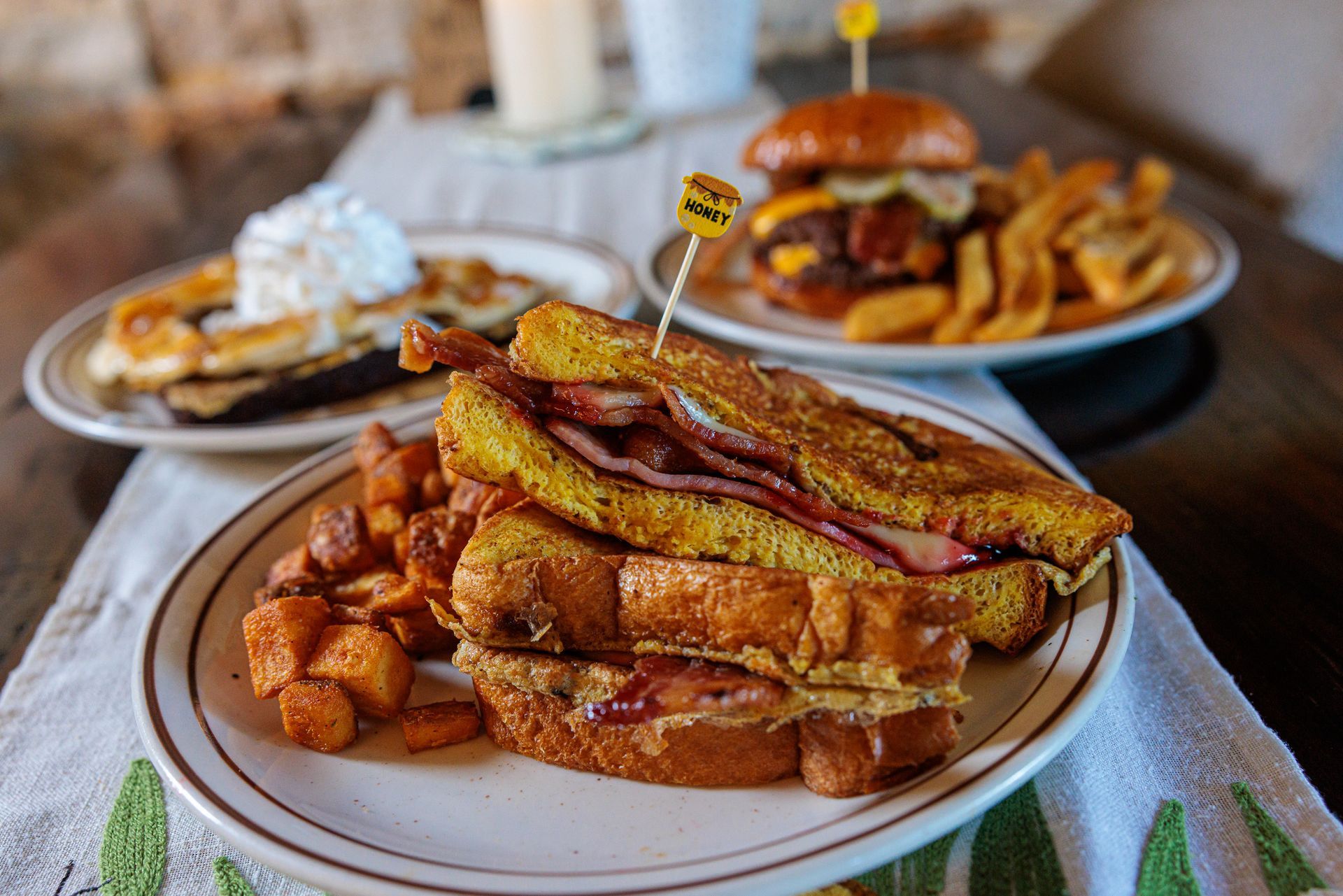 Plates of food: French toast sandwich, burger, waffles, and sweet potato cubes.