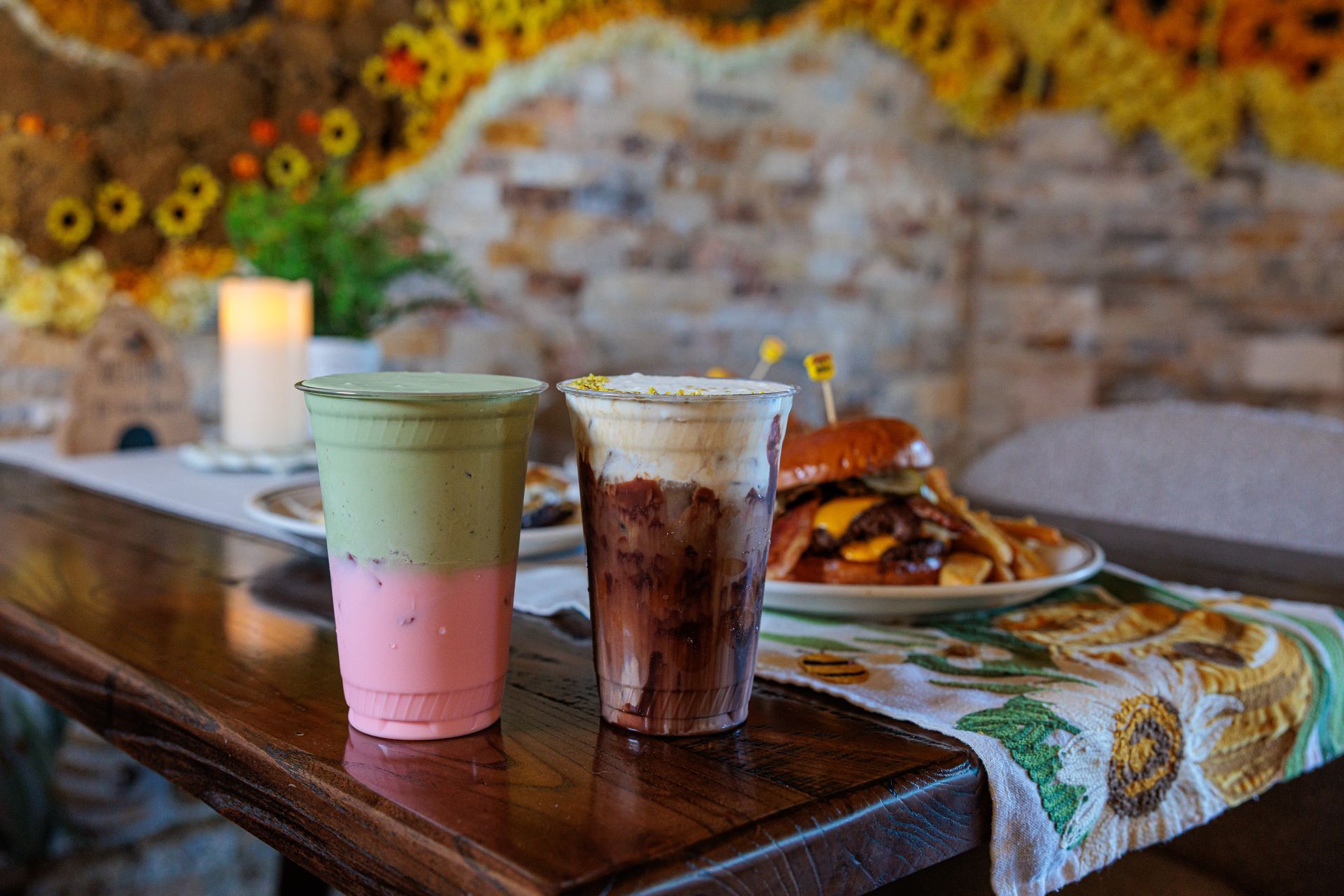 Two layered drinks, a burger, and fries on a table with sunflower decor.