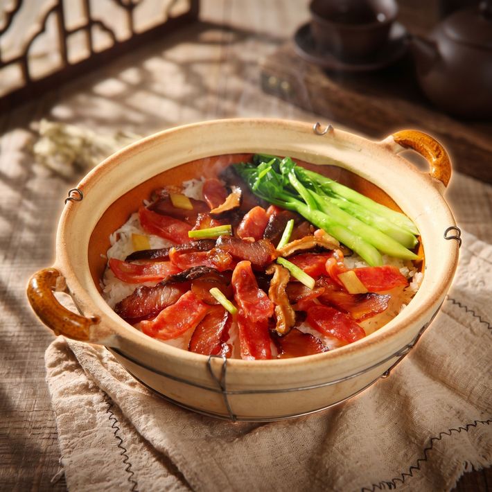Braised meat in a black clay pot with green onion garnish on a woven trivet