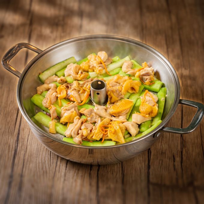 Braised meat and vegetables in a black clay pot on a woven placemat, with green onions in the background