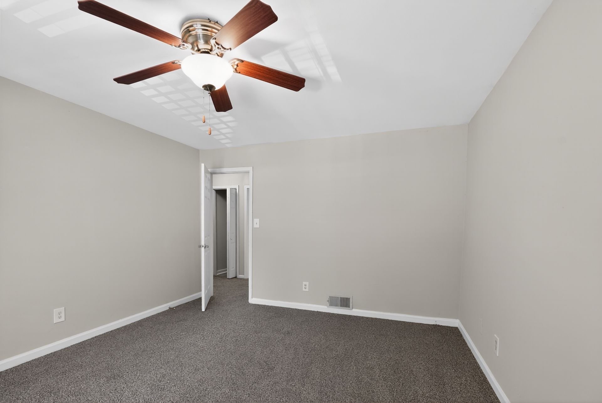 Empty gray bedroom with carpet, ceiling fan, and open doorway