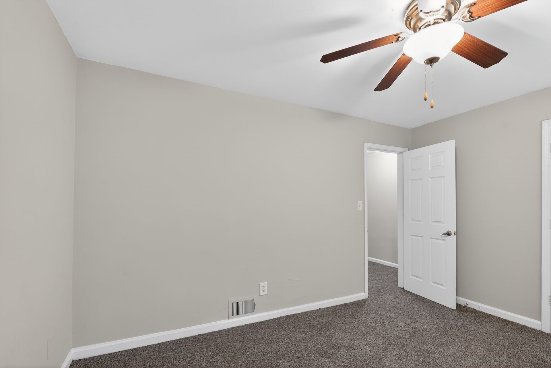Empty beige bedroom with carpet, ceiling fan, and open white closet door.
