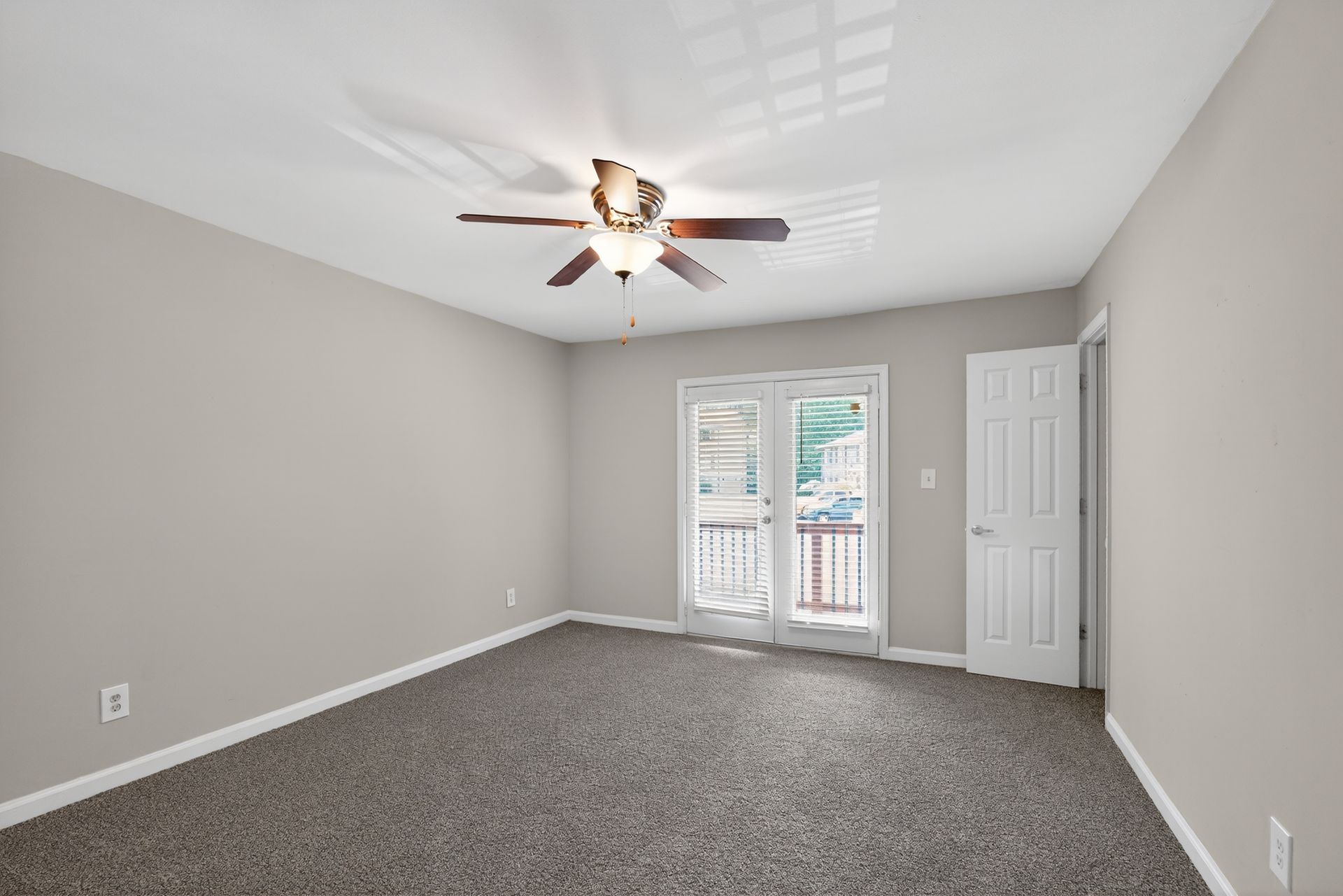 Empty gray bedroom with carpet, ceiling fan, and French doors leading outside
