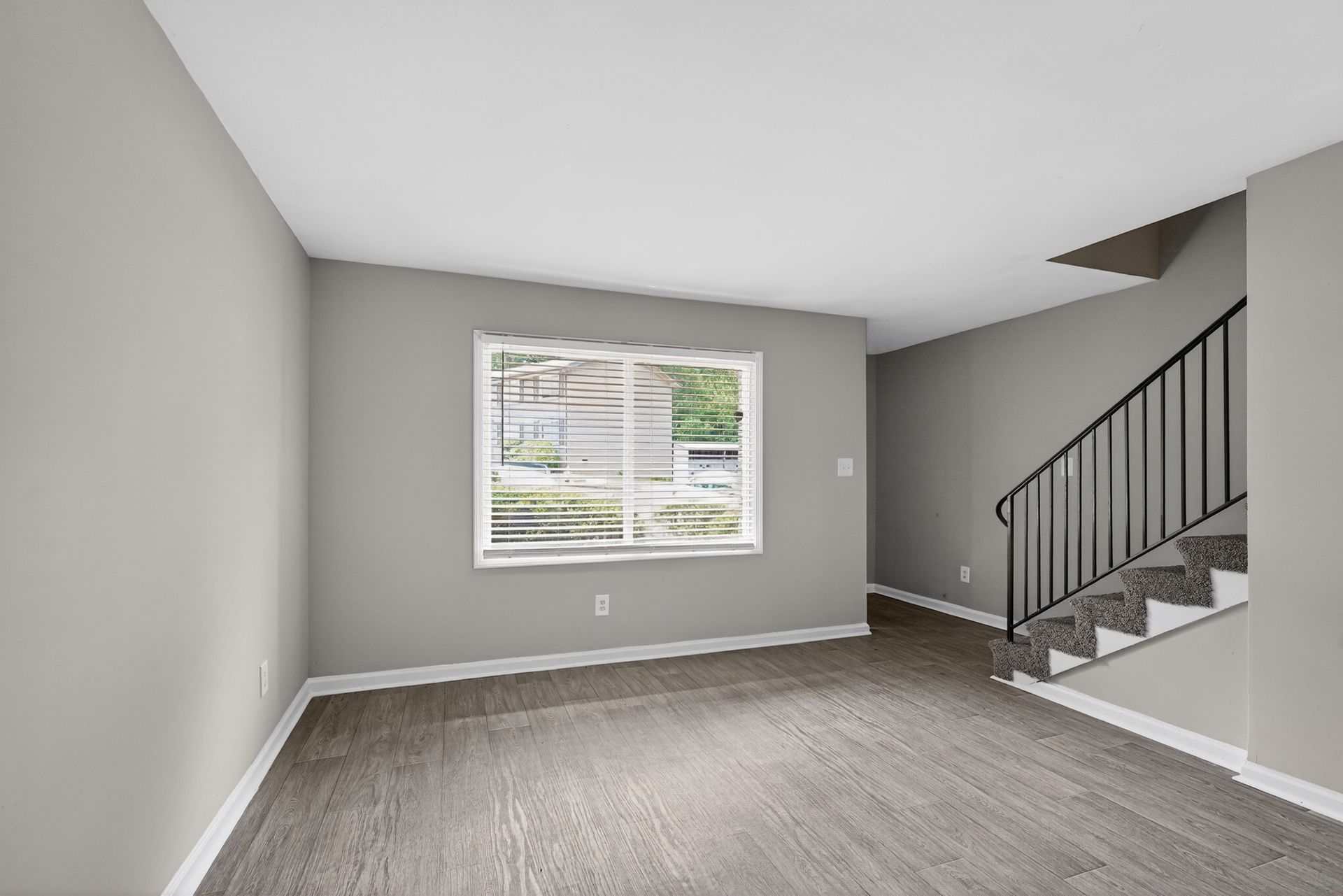 Empty gray living room with carpet, window, and staircase with black railing