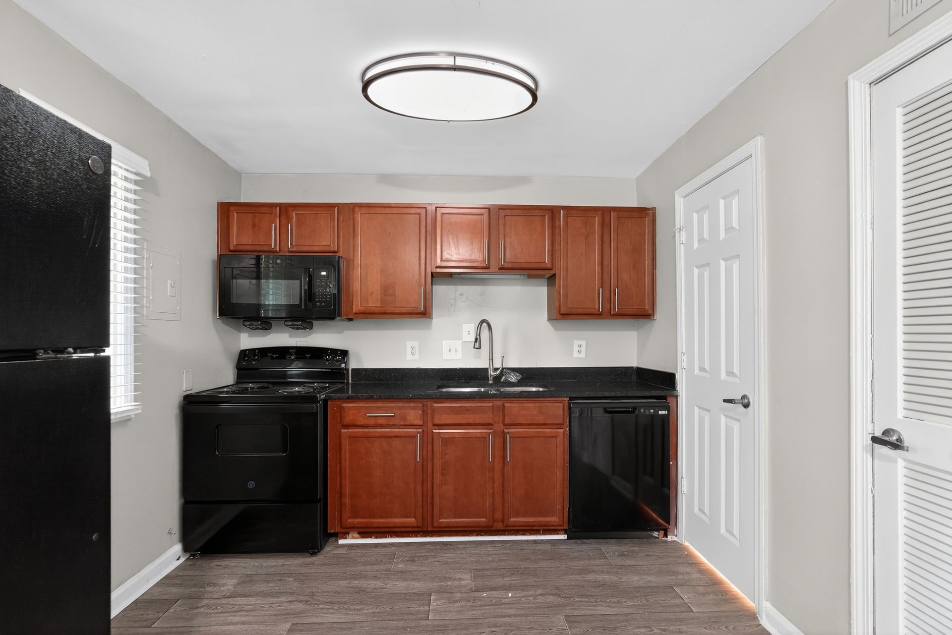 Small kitchen with black appliances, wood cabinets, white walls, and a window near the sink.
