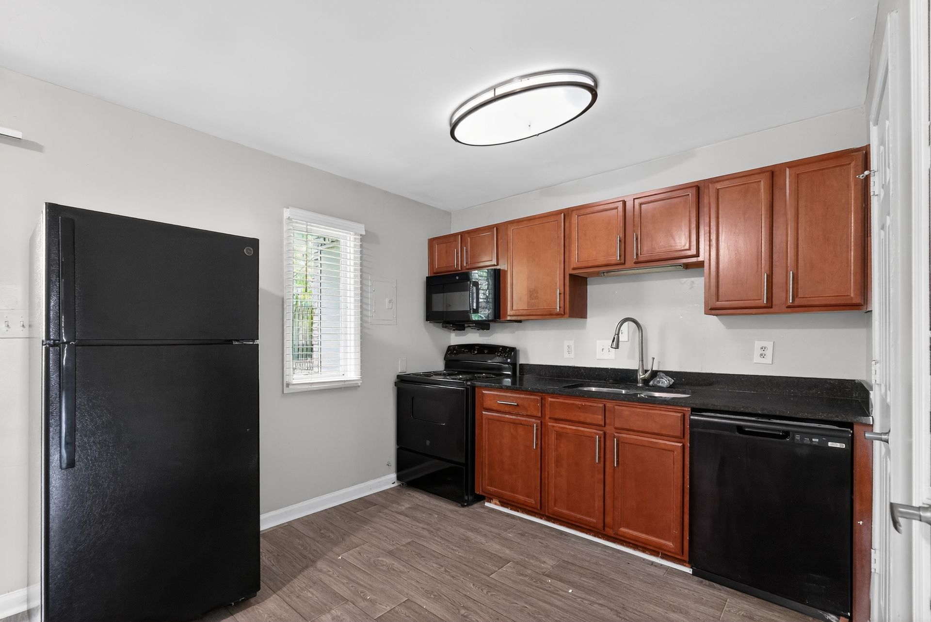 Compact kitchen with black appliances, wood cabinets, and a round ceiling light